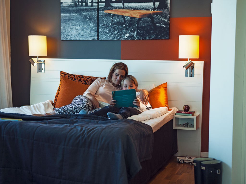 Familj läser bok i sovrum i Sky Hotel Apartments